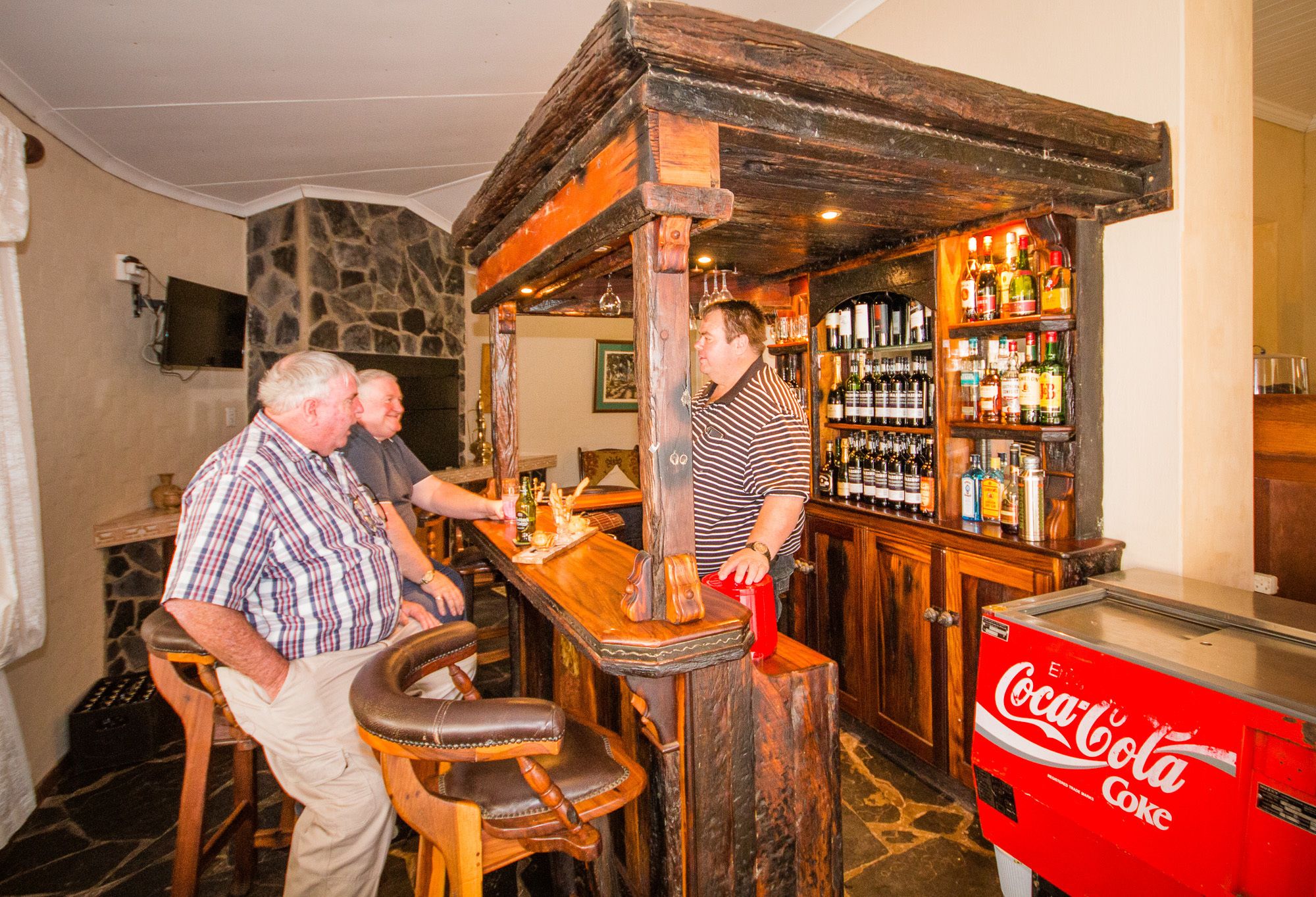 Ein Barbereich mit Holzzimmermöbeln, einer Steinwand und einem Coca-Cola-Kühlschrank.