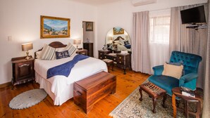 A hotel room with a large bed, a desk, a chair, a TV, and a painting on the wall.
