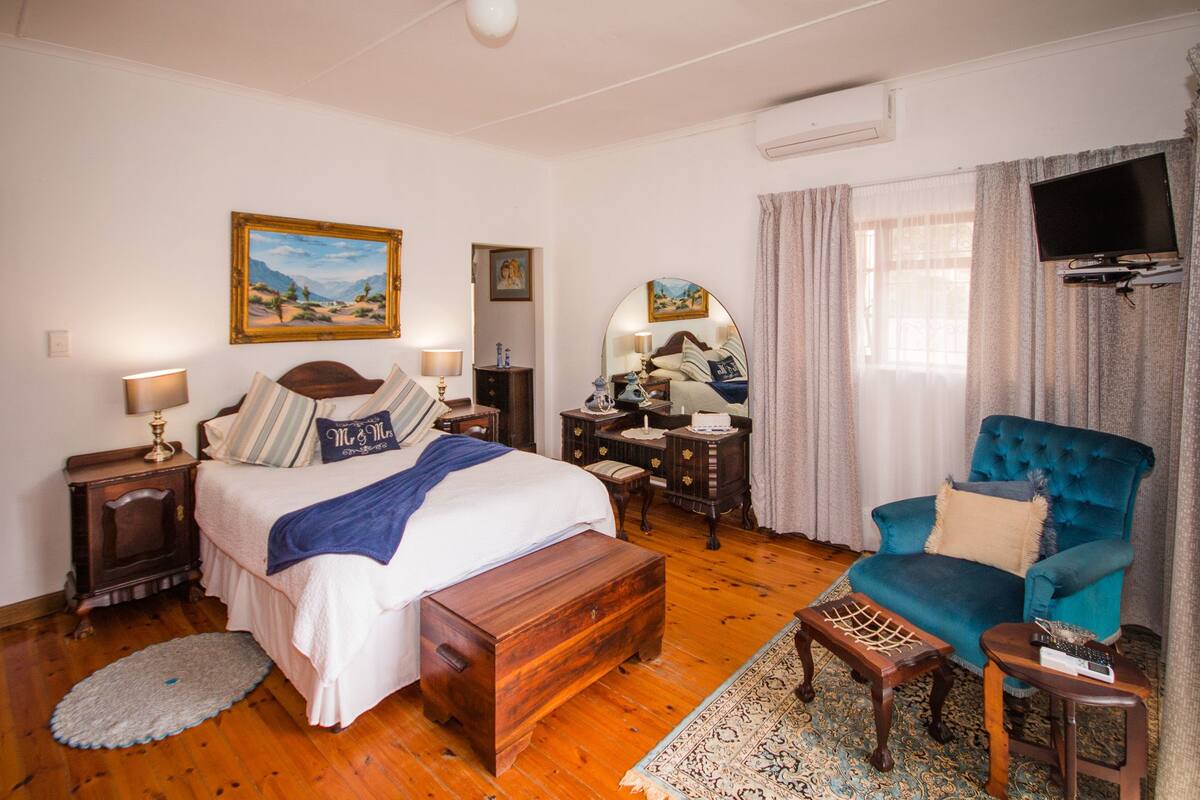 A hotel room with a large bed, a desk, a chair, a TV, and a painting on the wall.