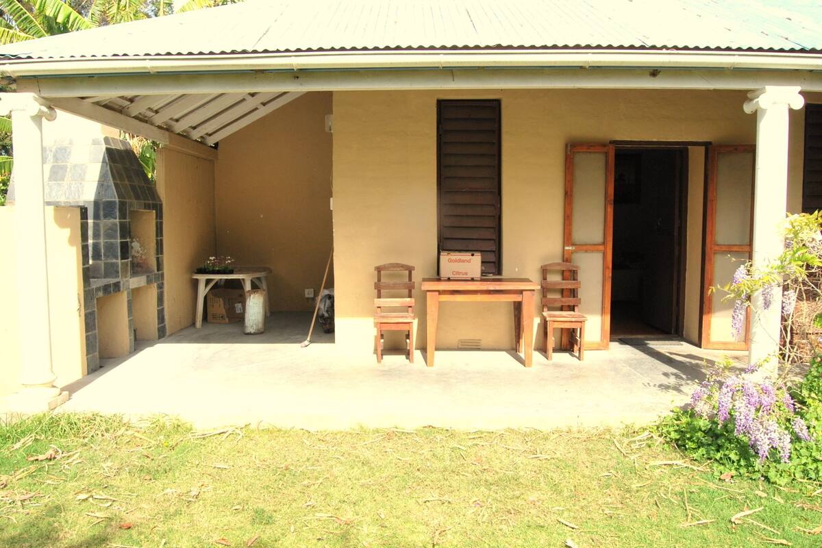 A covered outdoor area with a table and chairs, a small table with a potted plant, and a box labeled 'Goldland Citrus'.