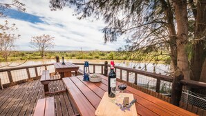 A wooden deck with picnic tables overlooking a river, surrounded by trees and a clear sky. - Homestead B & B (Addo)