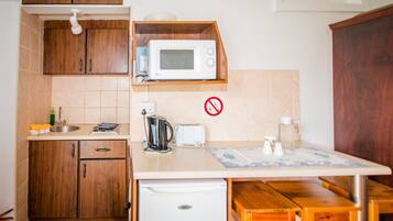 A compact kitchen with wooden cabinets, a microwave, a kettle, and a table with benches.