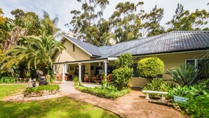 A two-story house with a covered porch, surrounded by lush greenery and a well-maintained garden. - Homestead B & B (Addo)