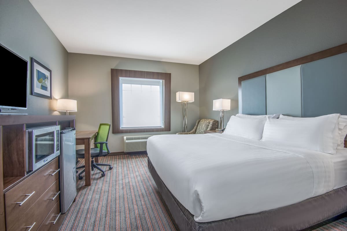 A hotel room with a large bed, a desk with a computer, a chair, and a television.