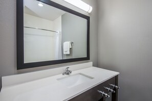 A bathroom with a large mirror, white sink, and dark cabinet with multiple faucets. - Holiday Inn Express & Suites Stillwater - University Area by IHG (Stillwater)