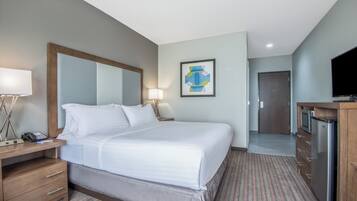 A hotel room with a bed, bedside table, lamp, artwork, and a television.