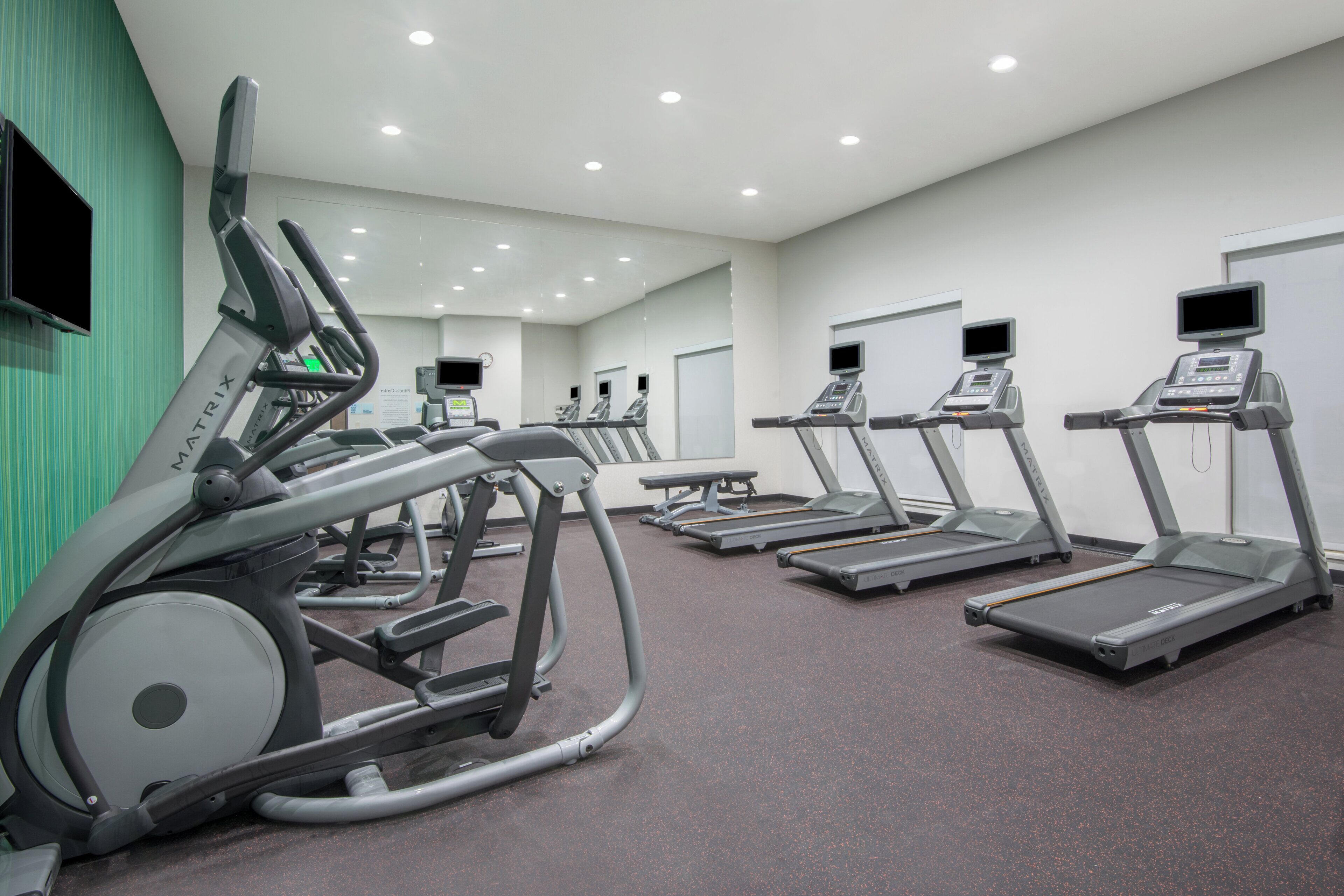 Une salle de sport équipée de tapis de course, de vélos d’appartement et d’appareils elliptiques.