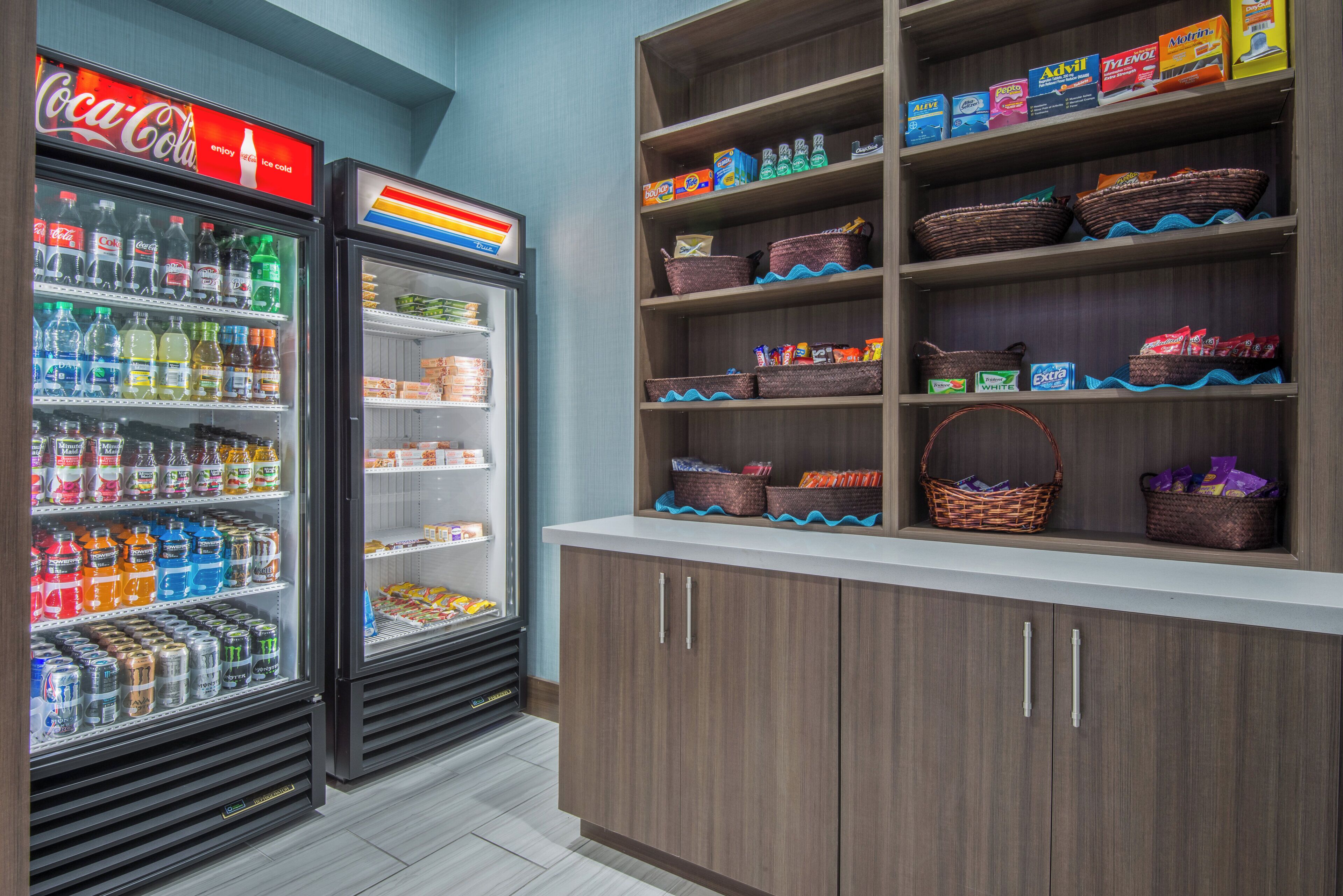 A beverage cooler stocked with various drinks and a shelf with baskets and snacks.