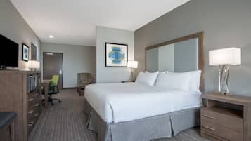 Una habitación de hotel con una cama grande, un escritorio con una silla, un televisor y un espejo.