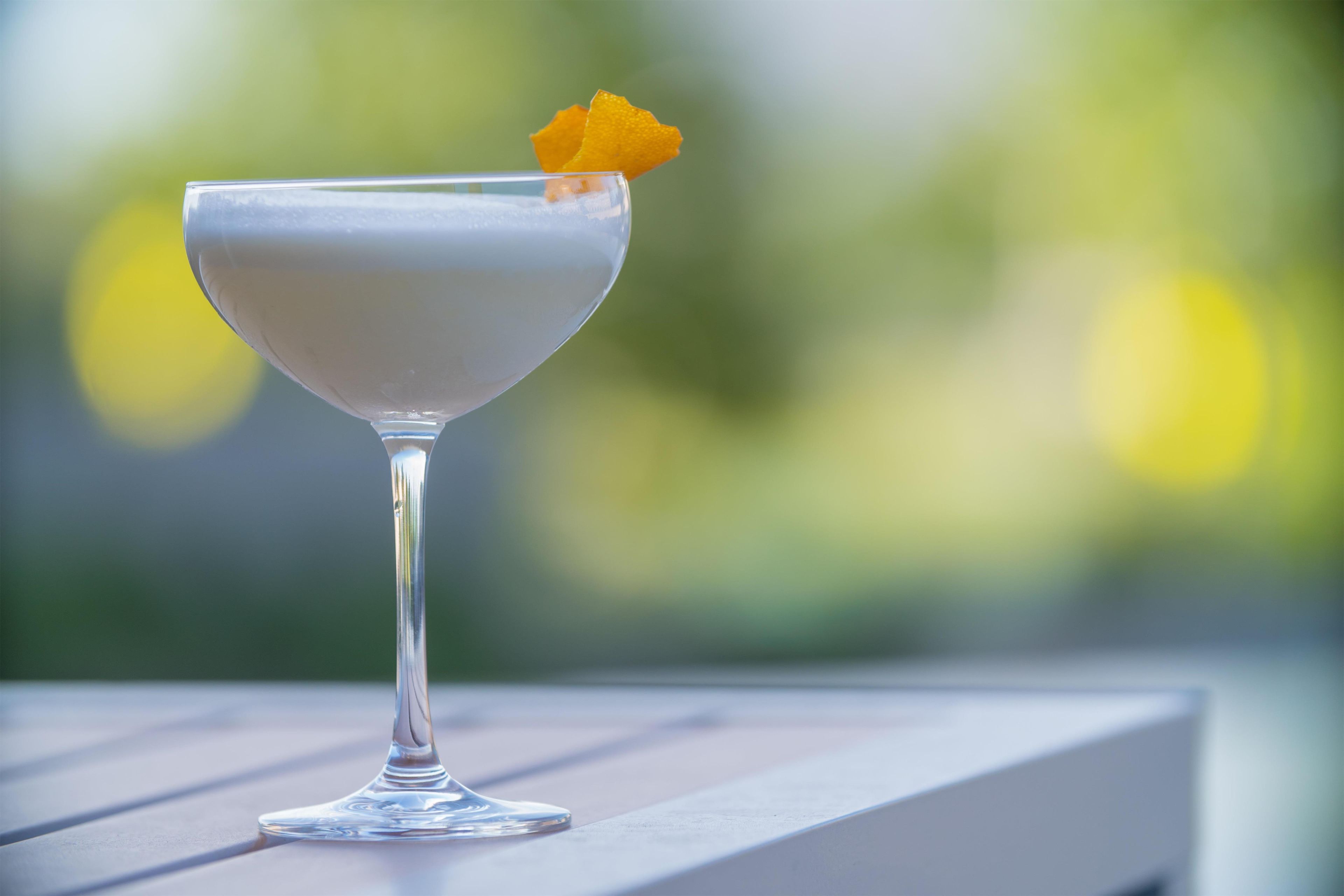 Ein klarer Cocktail mit Garnierung auf einer weißen Fläche.