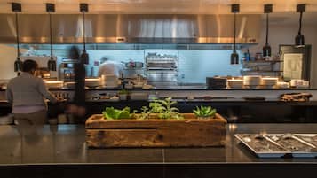 A modern kitchen with stainless steel appliances, hanging pendant lights, and a wooden planter with green plants on the counter.