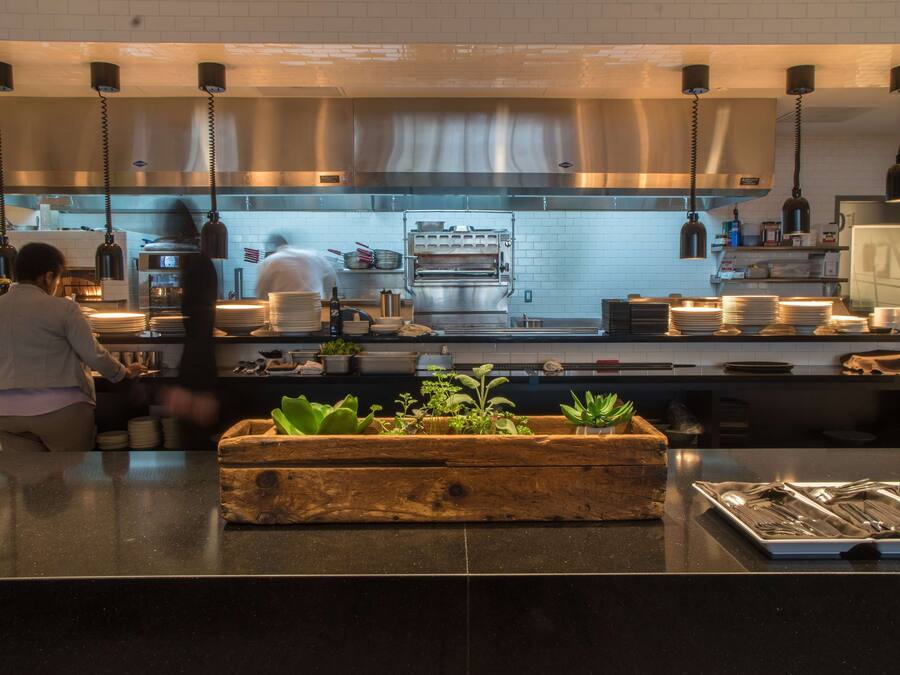 A modern kitchen with stainless steel appliances, hanging pendant lights, and a wooden planter with green plants on the counter.
