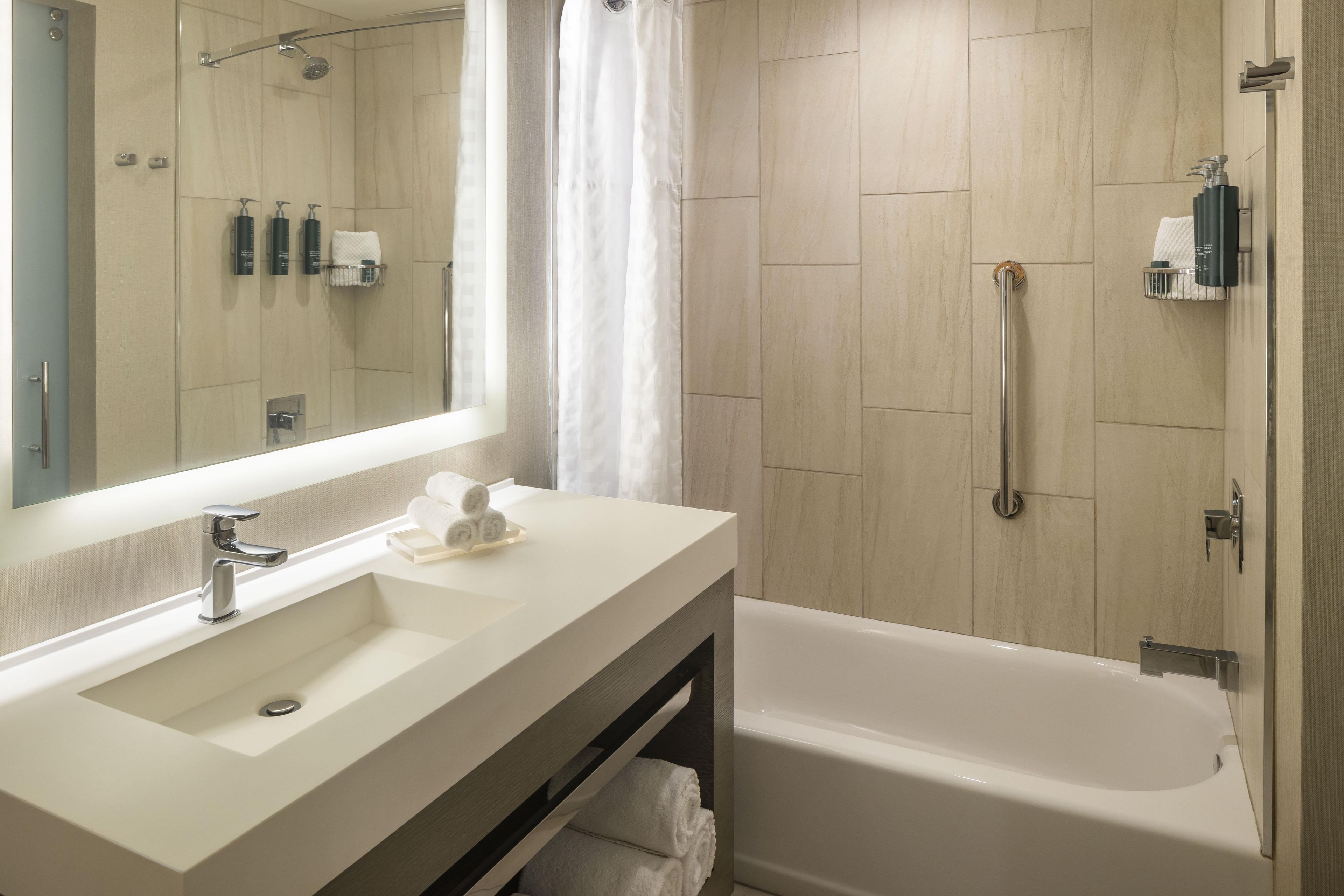 Ein modernes Badezimmer mit einem großen Spiegel, einem Waschbecken, einer Badewanne und einer Dusche inklusive Duschbrause.