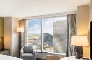 A hotel room with a large window, a sofa, a small table, and a lamp. - Hilton Cleveland Downtown (Cleveland)