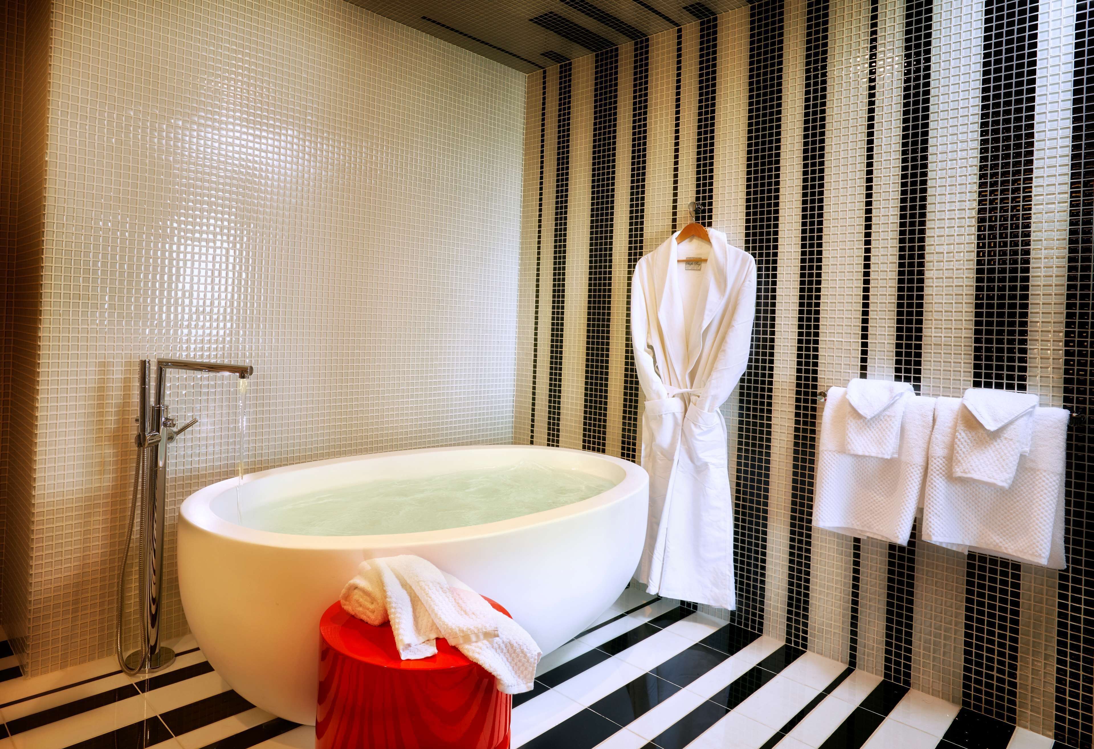Uma casa de banho moderna com uma banheira grande, um banquinho vermelho e uma barra de toalhas com toalhas.