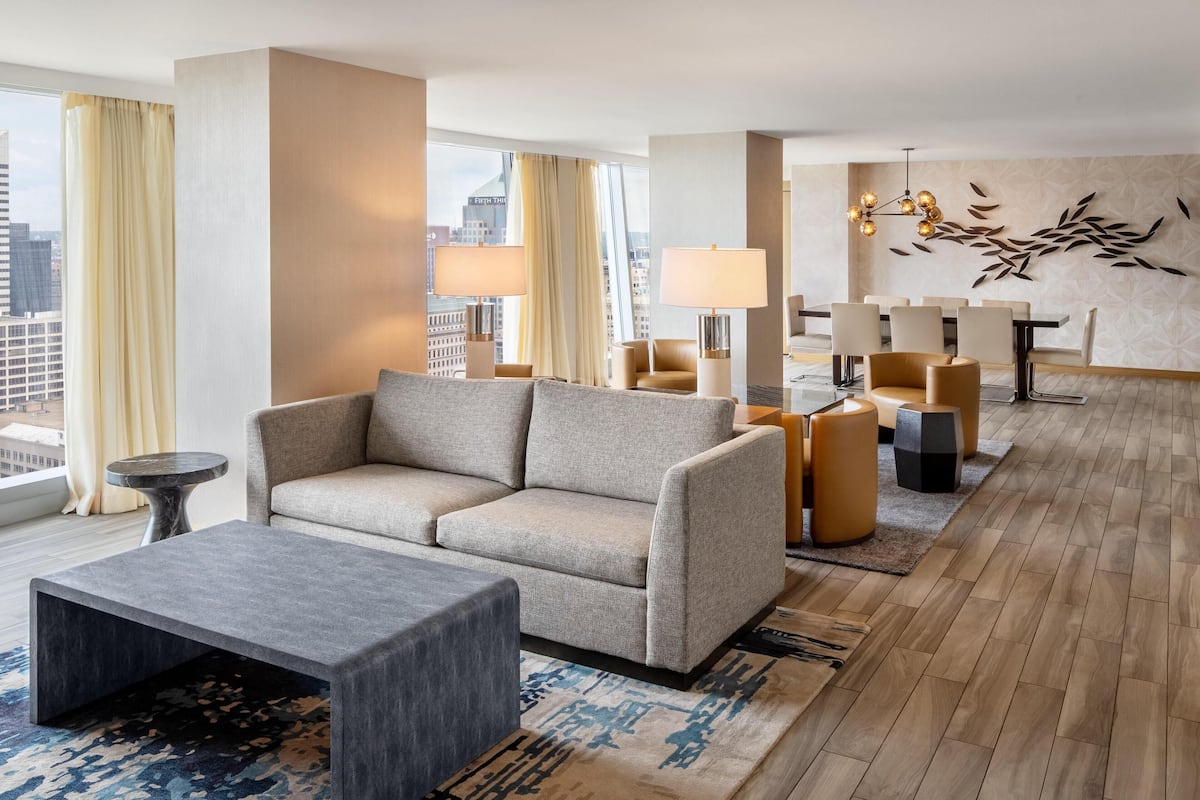 A modern hotel lobby with a sofa, armchairs, a coffee table, and a dining area.