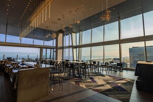 A modern dining area with high ceilings, large windows, and a view of the cityscape.