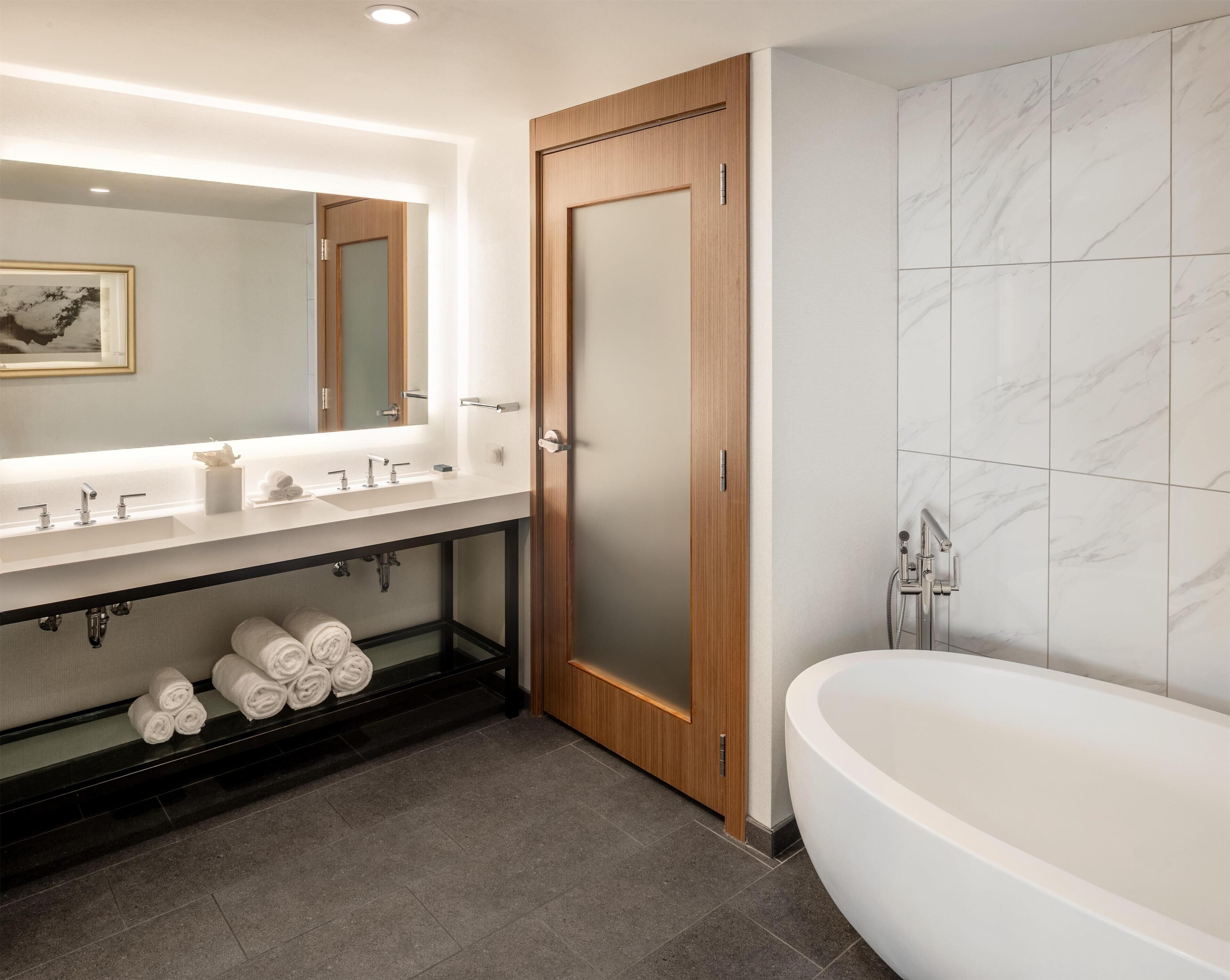 Une salle de bain moderne dotée d’une grande baignoire sur pieds, d’un meuble-lavabo à deux vasques et de murs recouverts de carreaux de marbre.