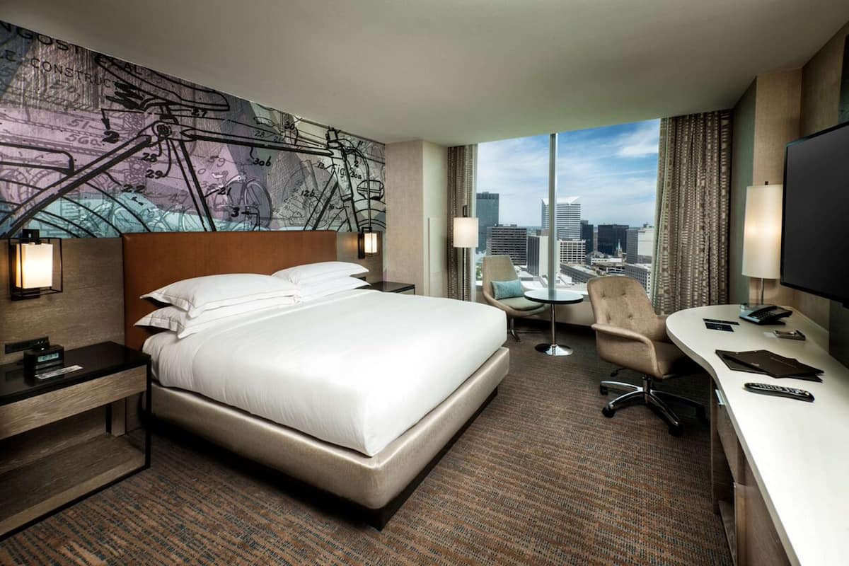 A hotel room with a large bed, a desk, a chair, a TV, and a city view.