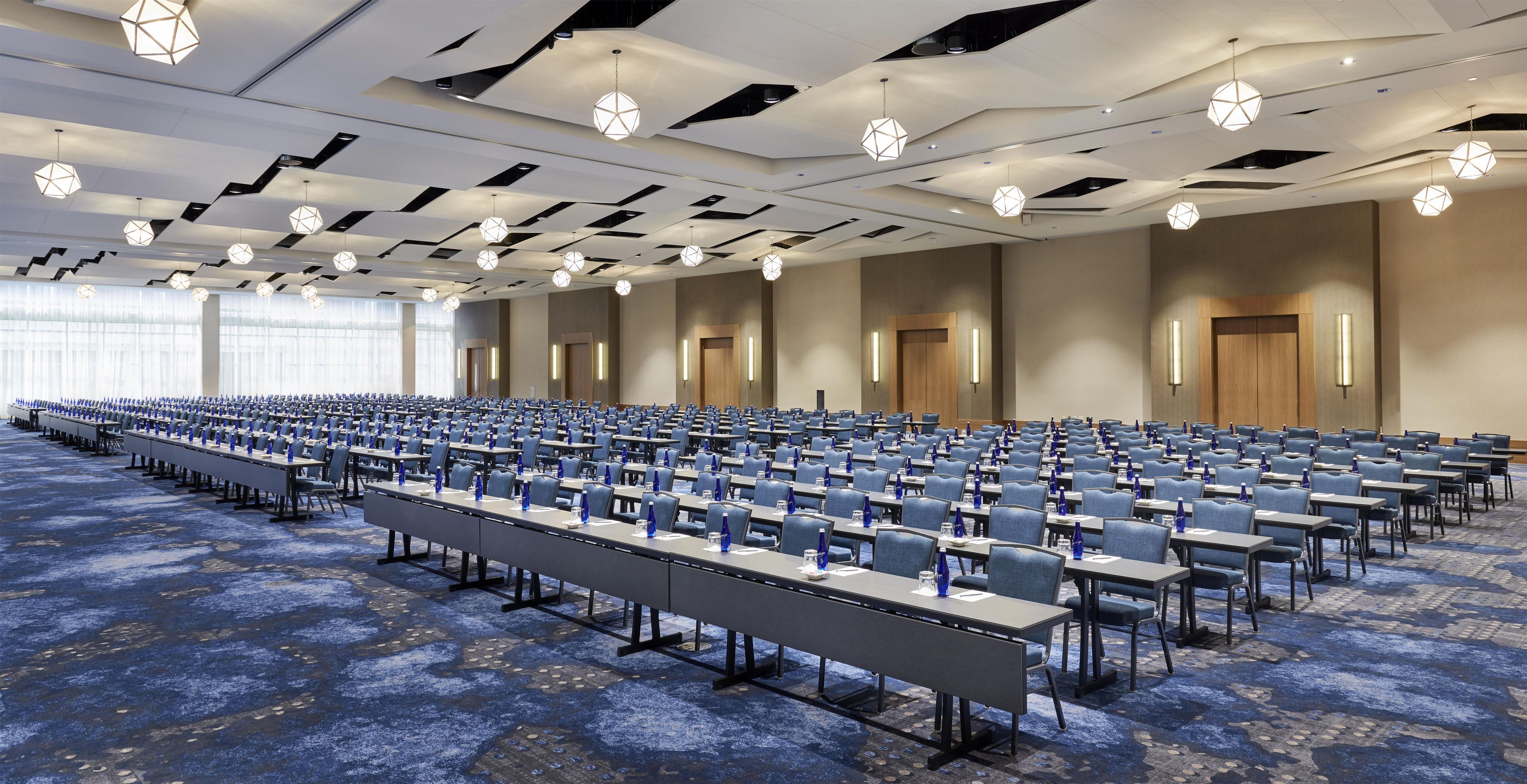A large conference room with rows of tables and chairs, a patterned carpet, and geometric ceiling lights.