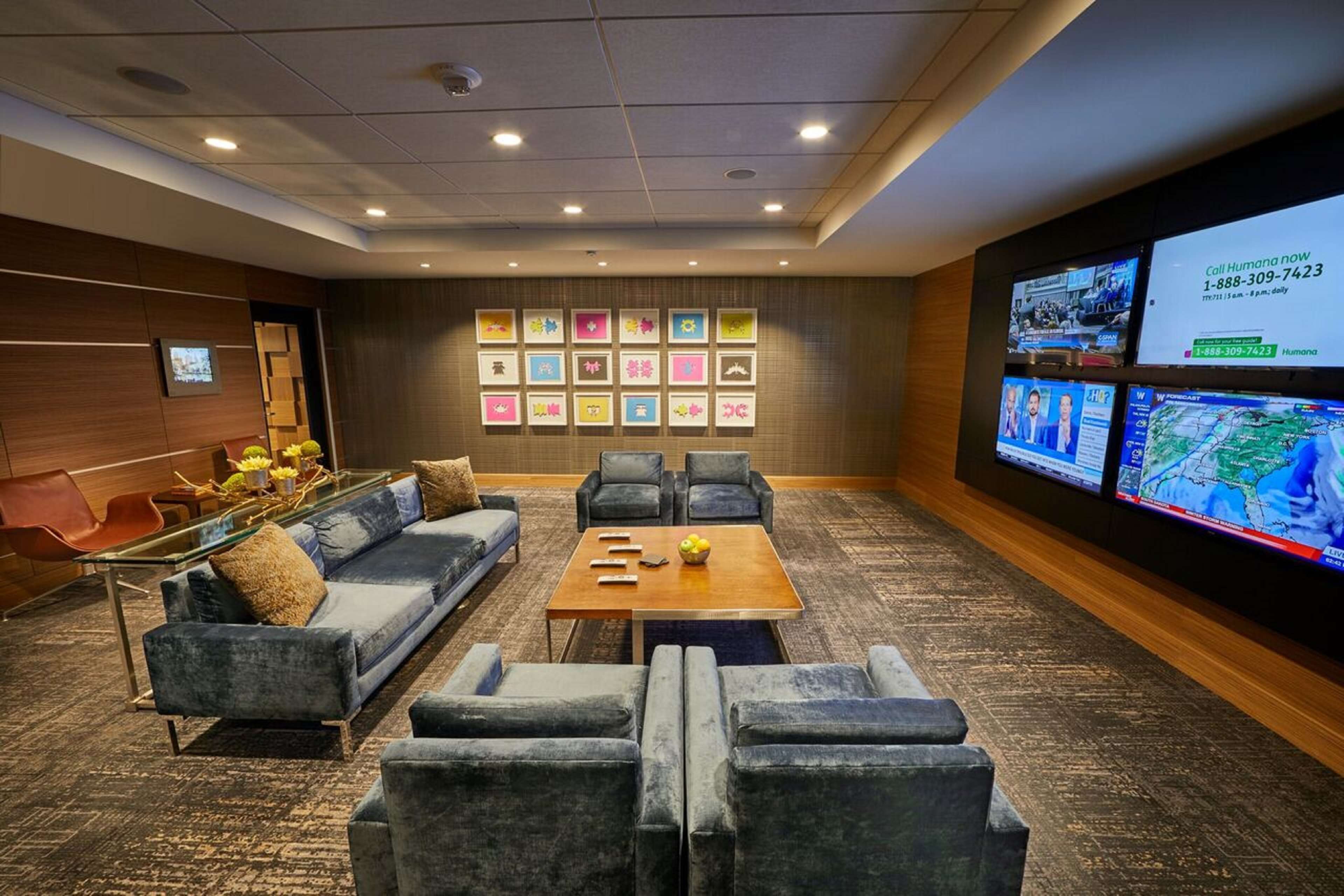 A conference room with a sofa, chairs, a coffee table, and a TV screen displaying a news channel.