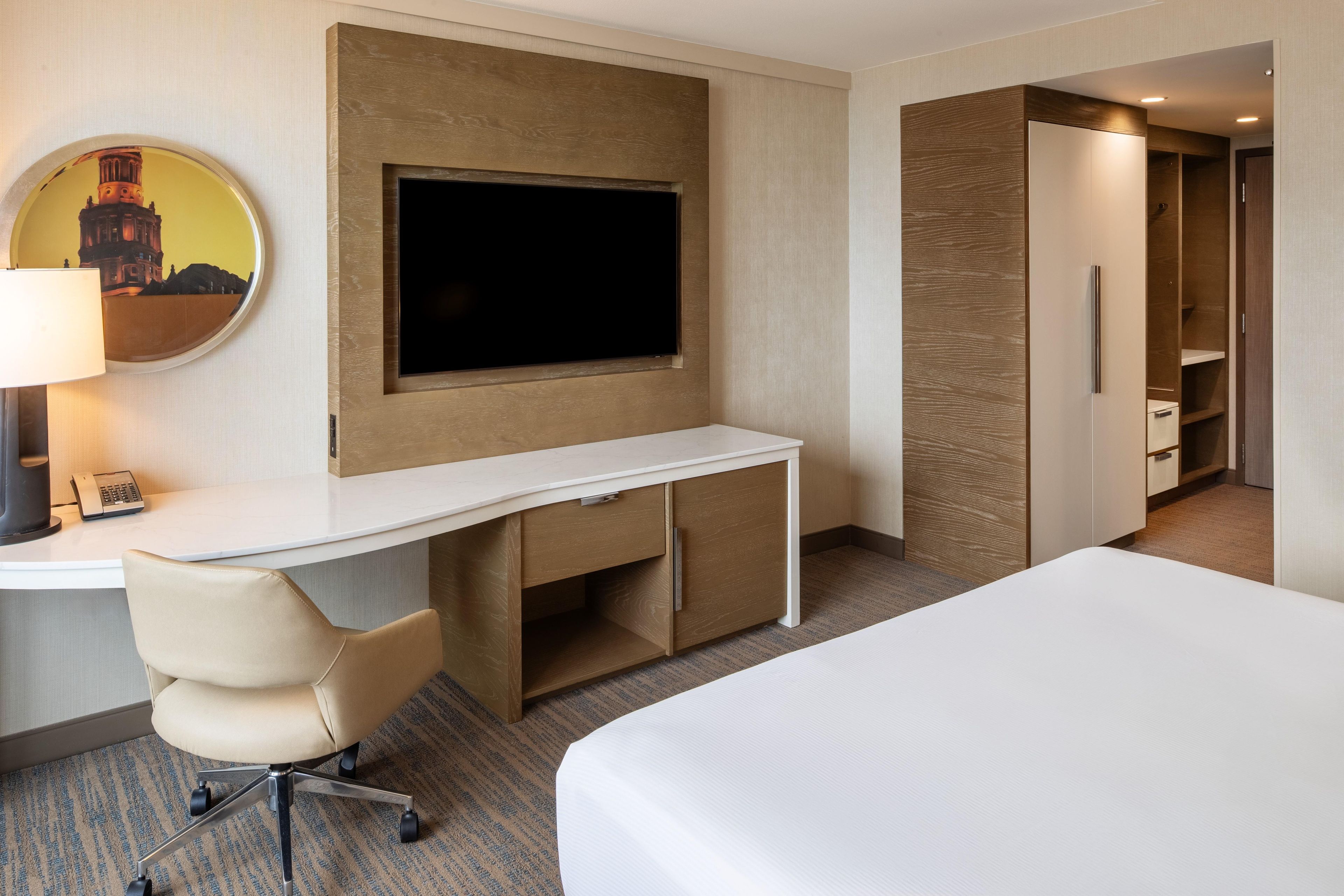 Habitación de hotel con cama, escritorio con silla, televisor de pantalla plana en la pared y armario.
