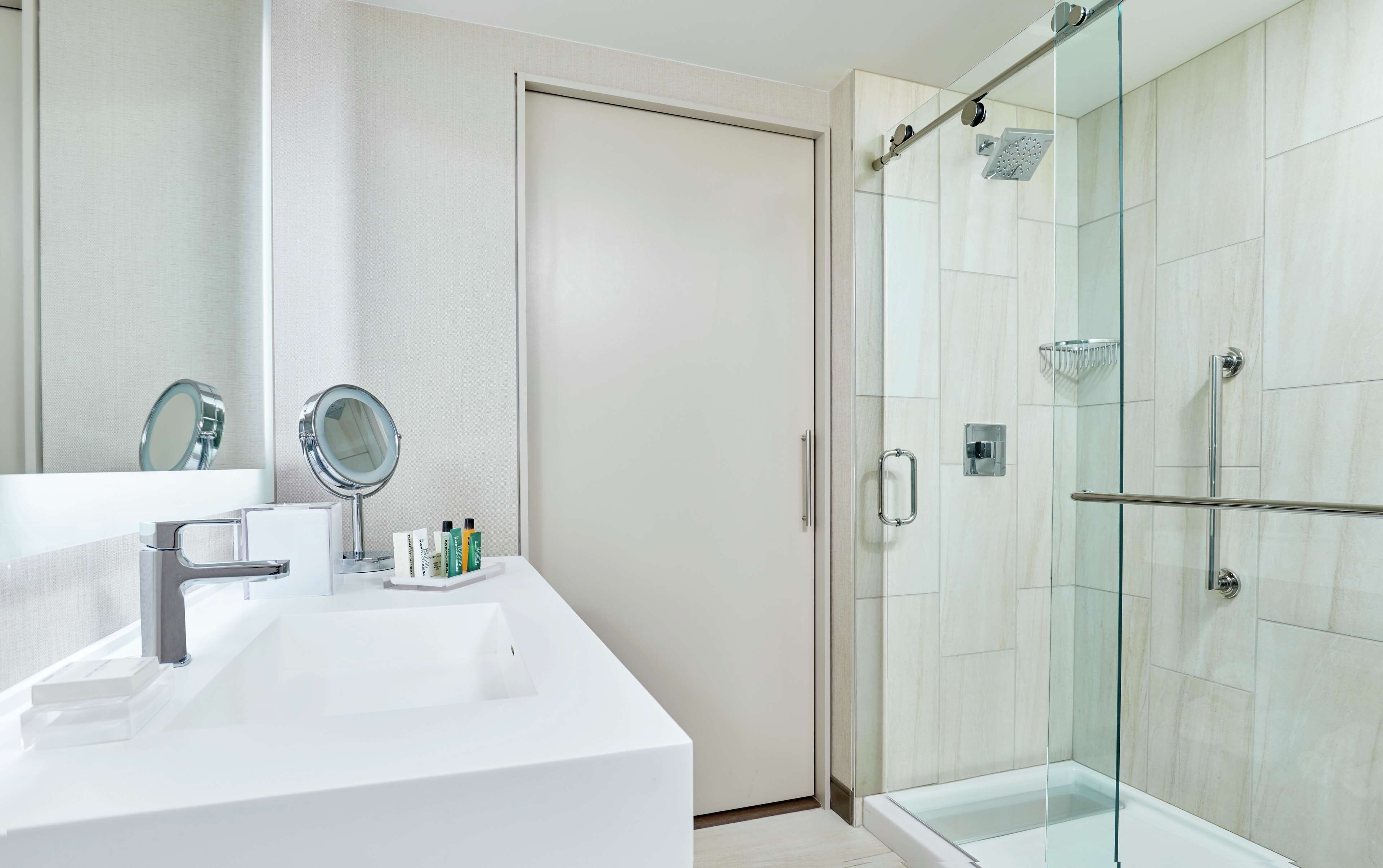 A modern bathroom with a white sink, a round mirror, and a glass-enclosed shower.
