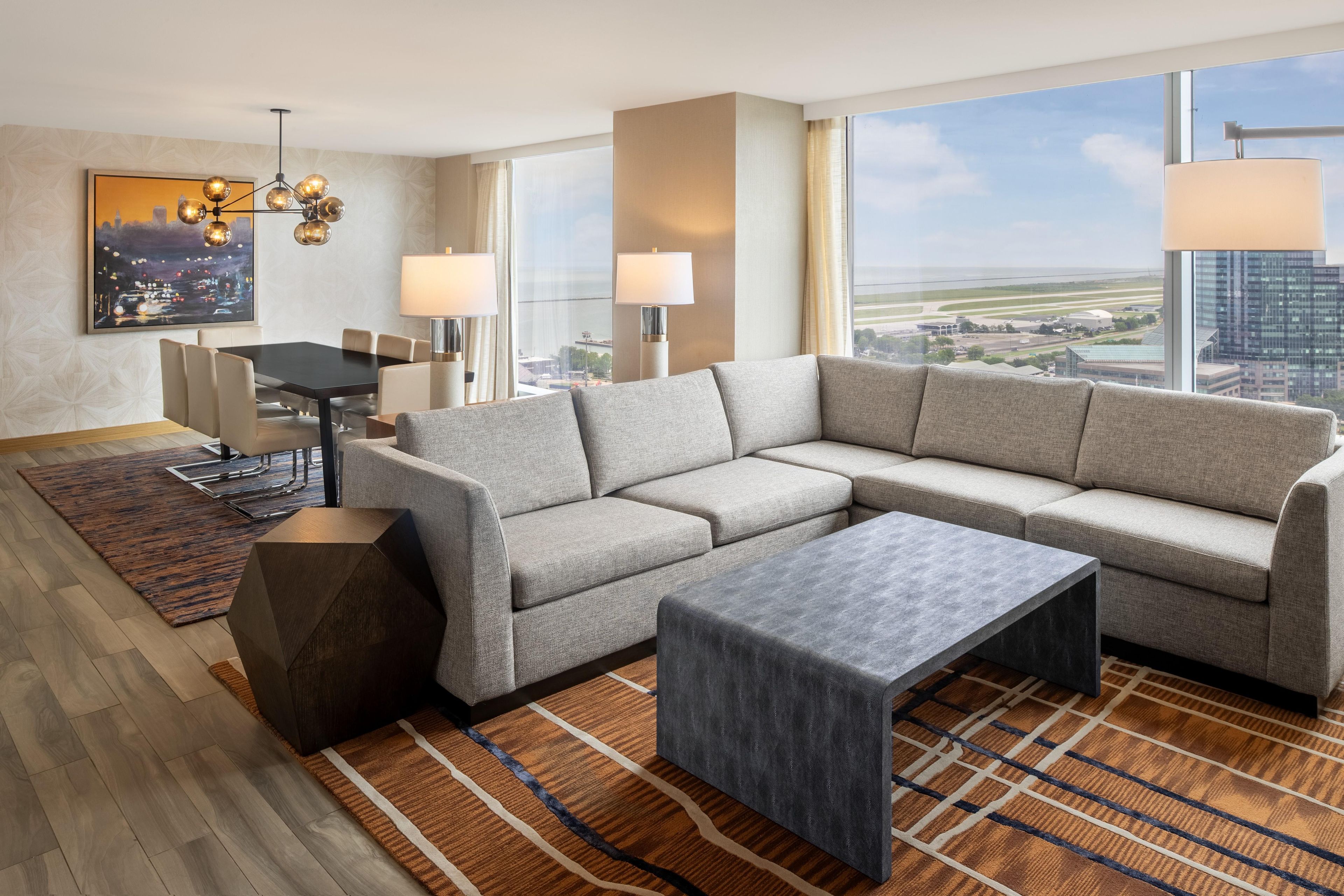 Una habitación de hotel moderna con un amplio sofá modular, una mesa de comedor y vistas a la ciudad.