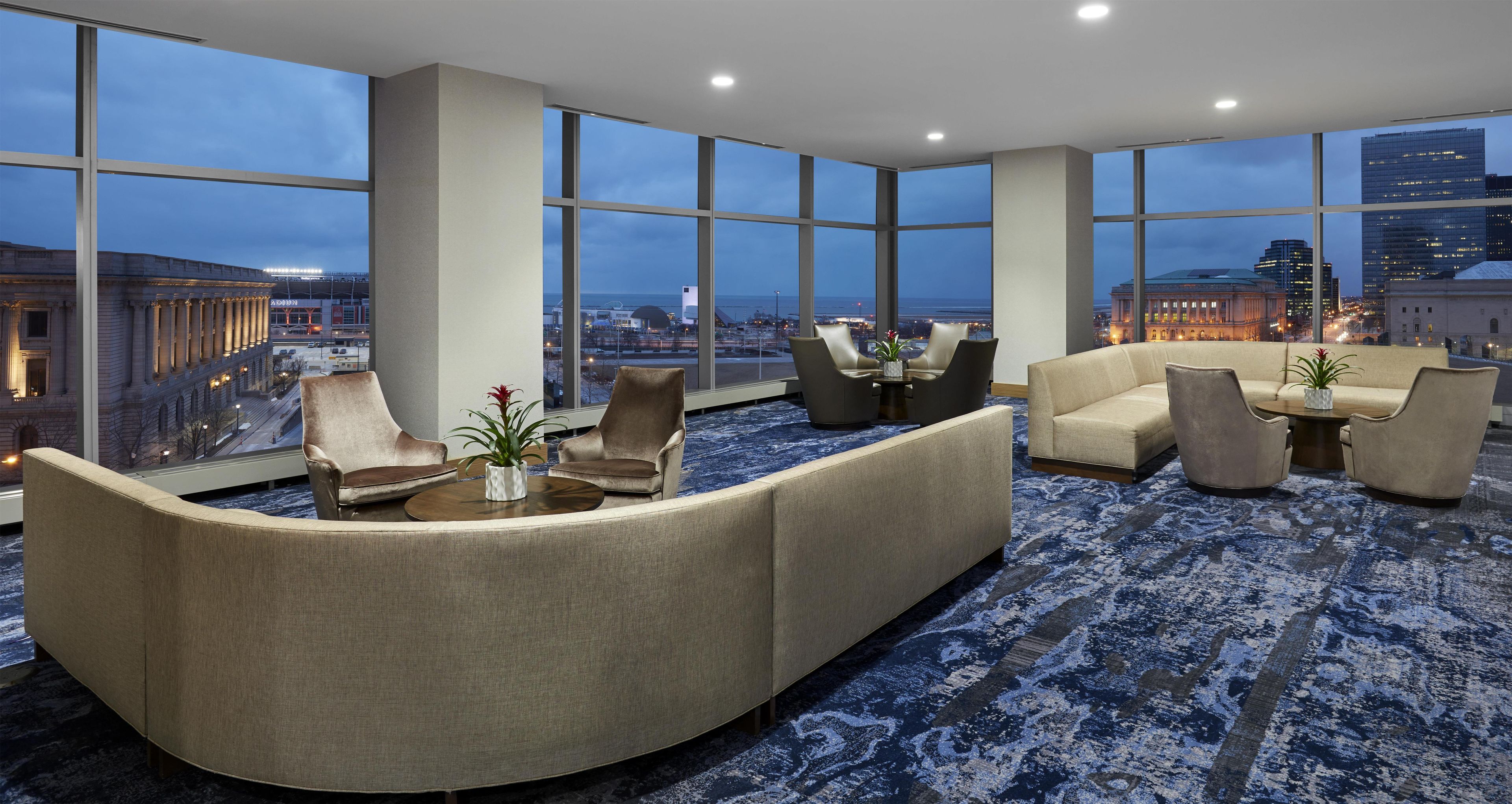 A spacious lounge with a large window offering a city view, a curved sofa, and a small coffee table with a plant.