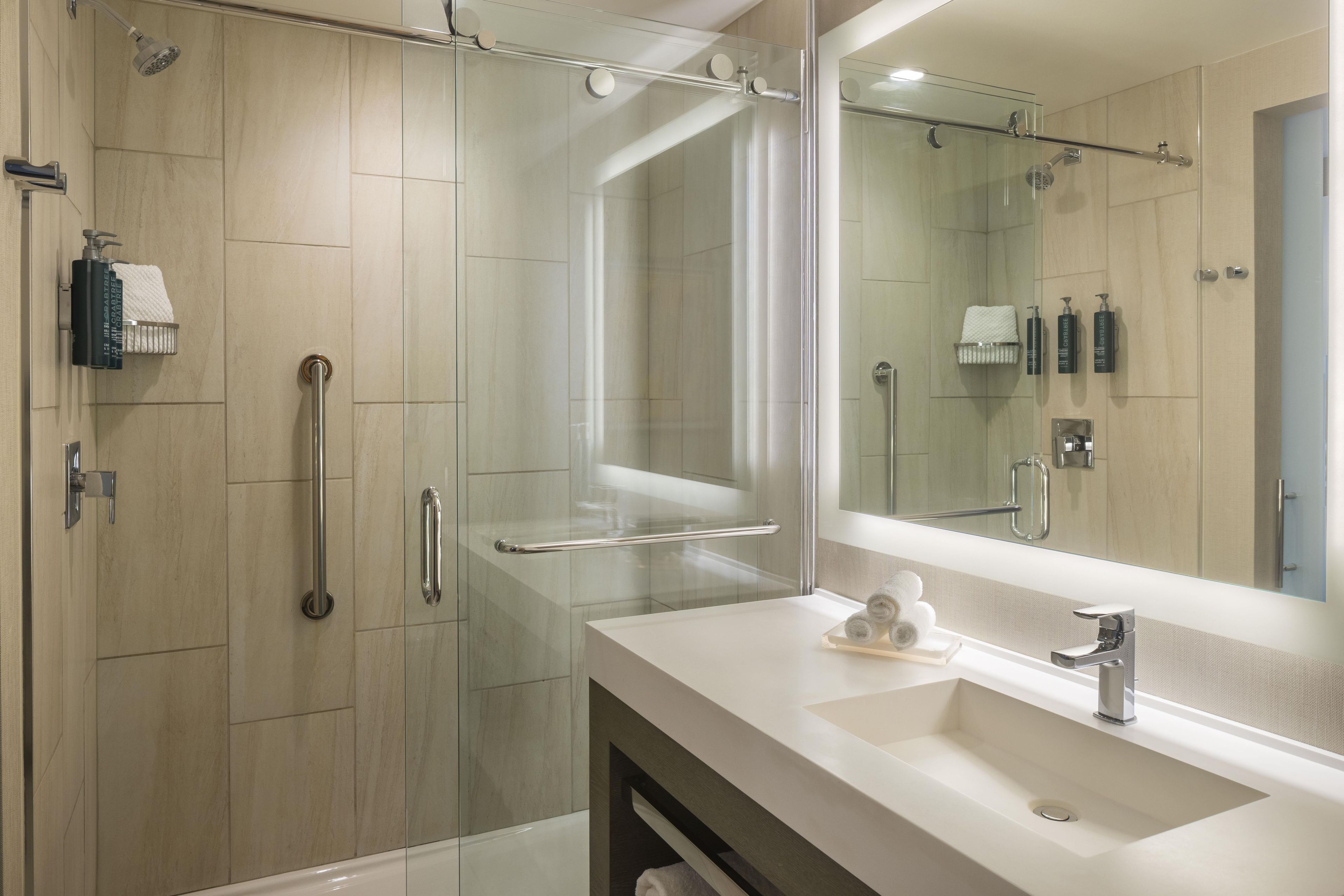 A modern bathroom with a glass-enclosed shower, a white sink, and a large mirror.