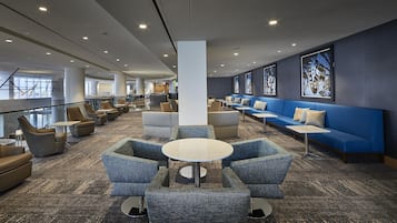 A modern lounge area with seating arrangements, a central table, and a view of the outside.