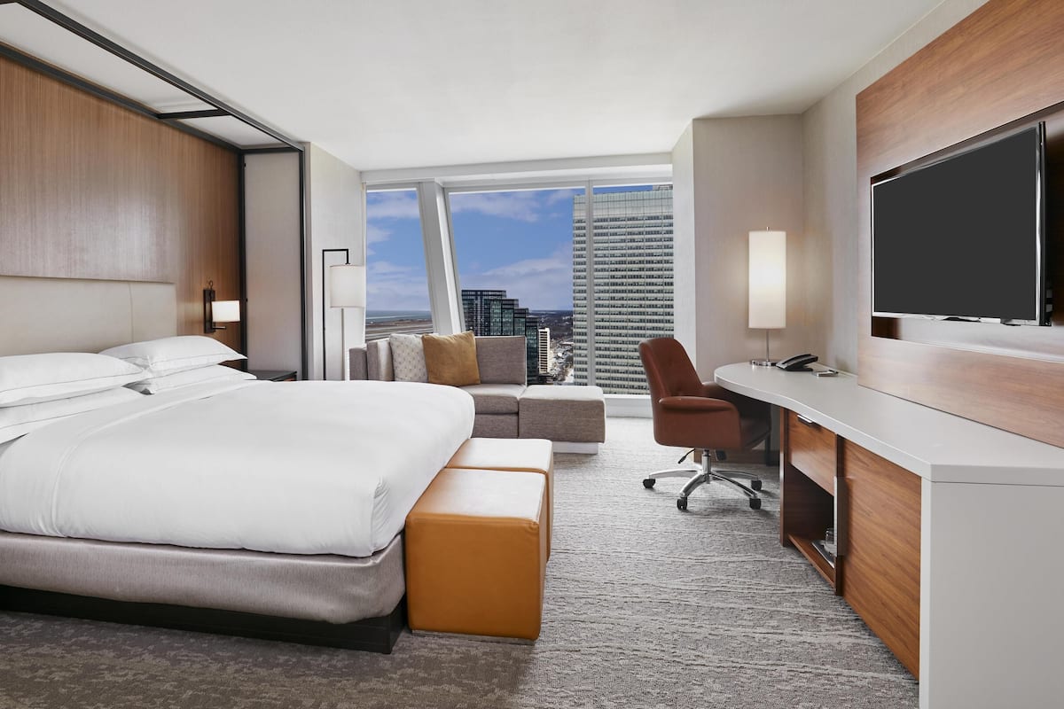 A modern hotel room with a large bed, a desk, a chair, and a TV.
