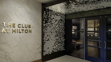 Una entrada de hotel moderna con una pared de mármol, un letrero que dice 'THE CLUB AT HILTON' y un panel luminoso decorativo.