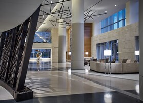 A spacious lobby with a modern design, featuring a large abstract sculpture, a seating area with sofas, and large windows providing natural light.