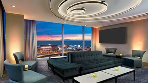 A modern hotel room with a large window offering a city view, a comfortable seating area with a sofa and chairs, a flat-screen TV, and ambient lighting. - Hilton Cleveland Downtown (Cleveland)