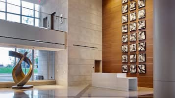 A modern lobby with a glass wall, a sculpture, and a wall of framed photographs.