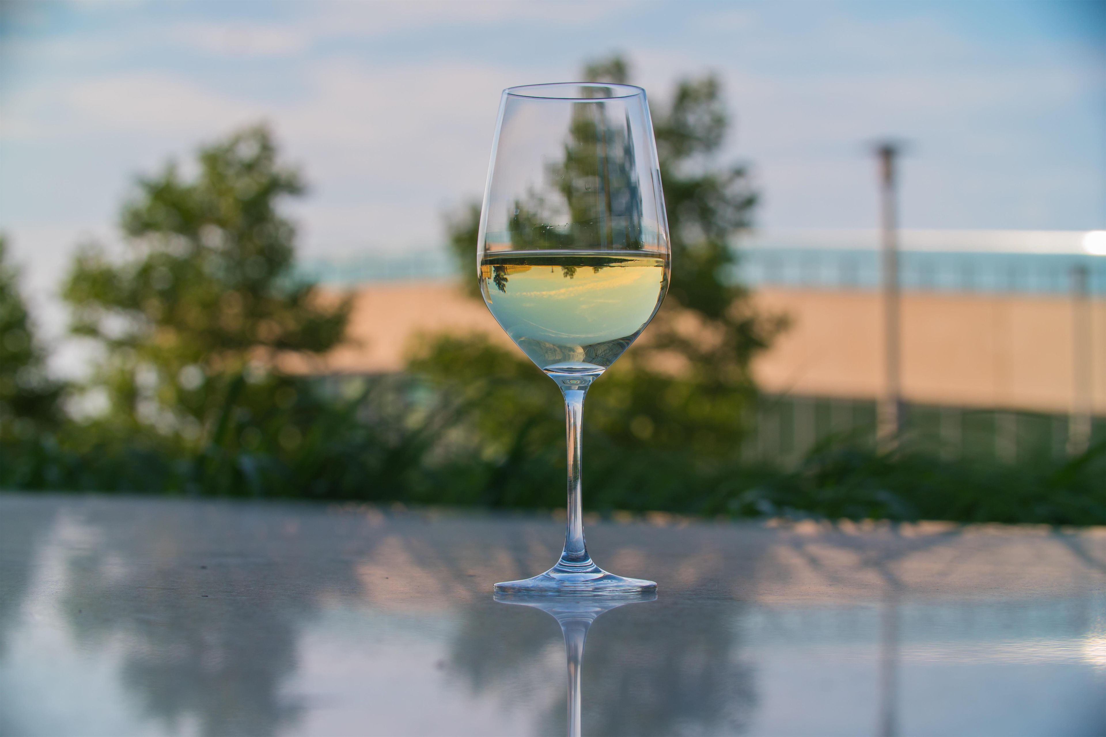 Una copa de vino blanco sobre una superficie reflectante, con un fondo exterior desenfocado.