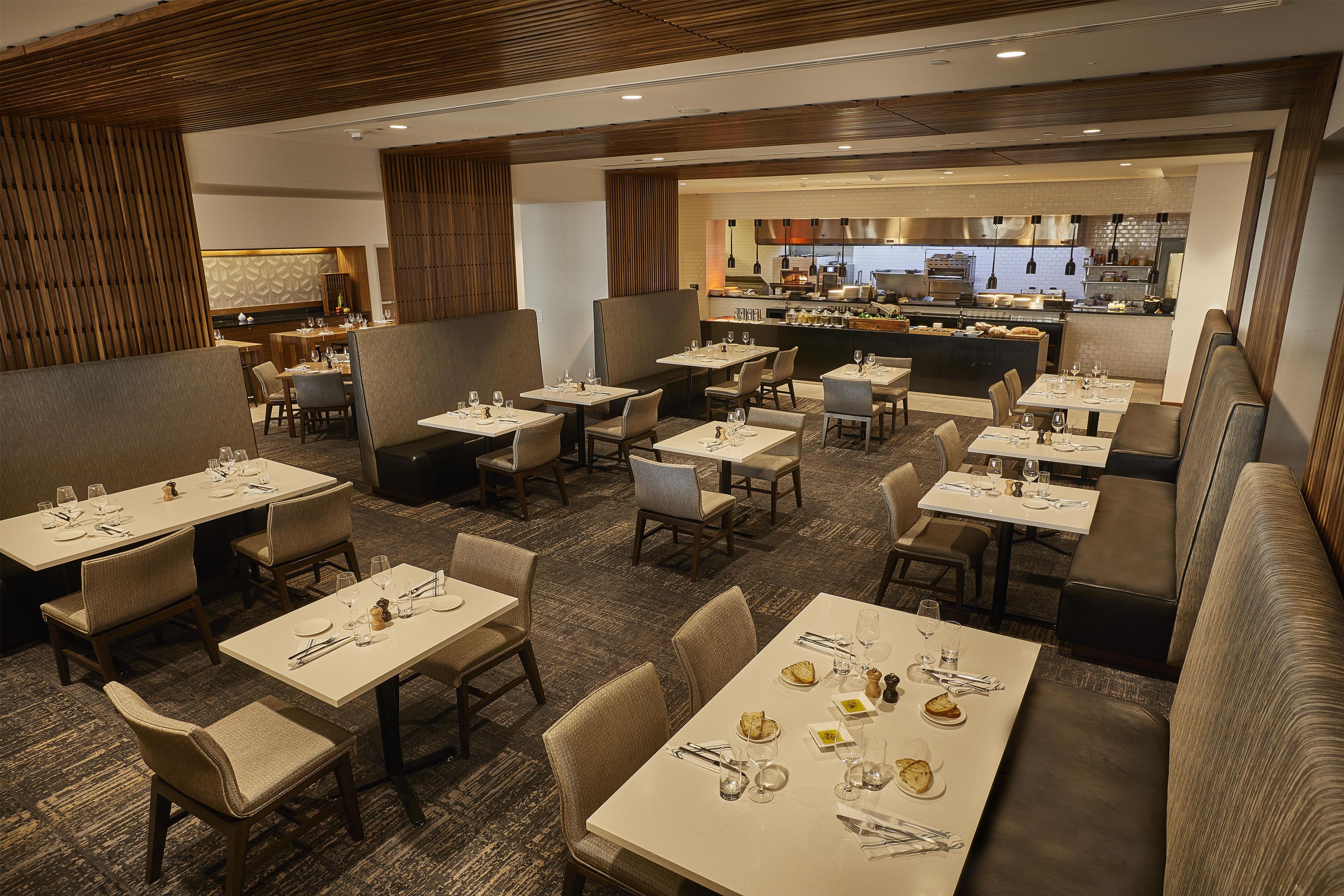 Un restaurant doté de nombreuses tables et de plusieurs coins repas, avec une cuisine située au fond de la salle et un tapis à motifs.