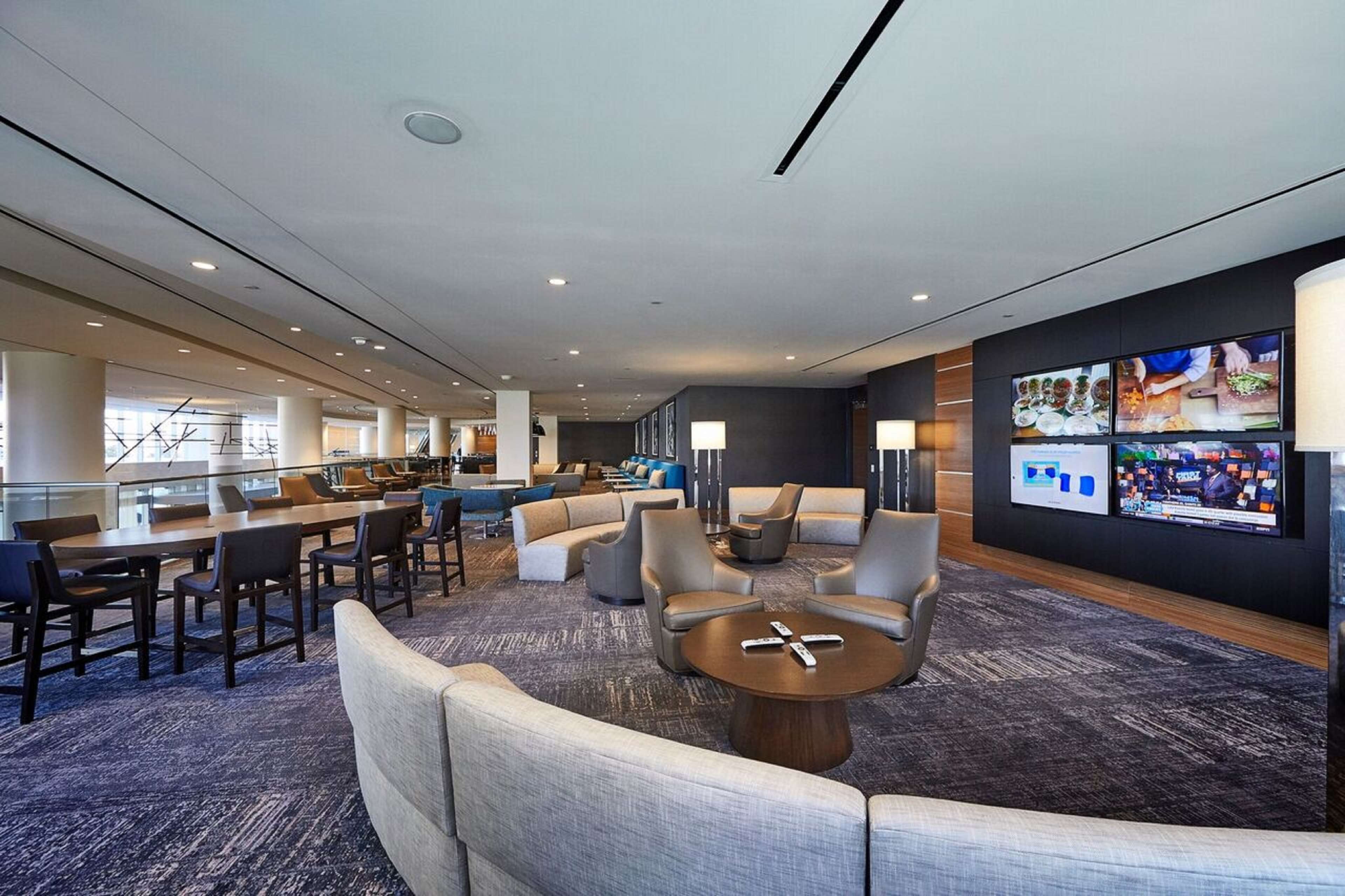 A modern hotel lobby with a long reception desk, comfortable seating areas, and a large digital menu display.