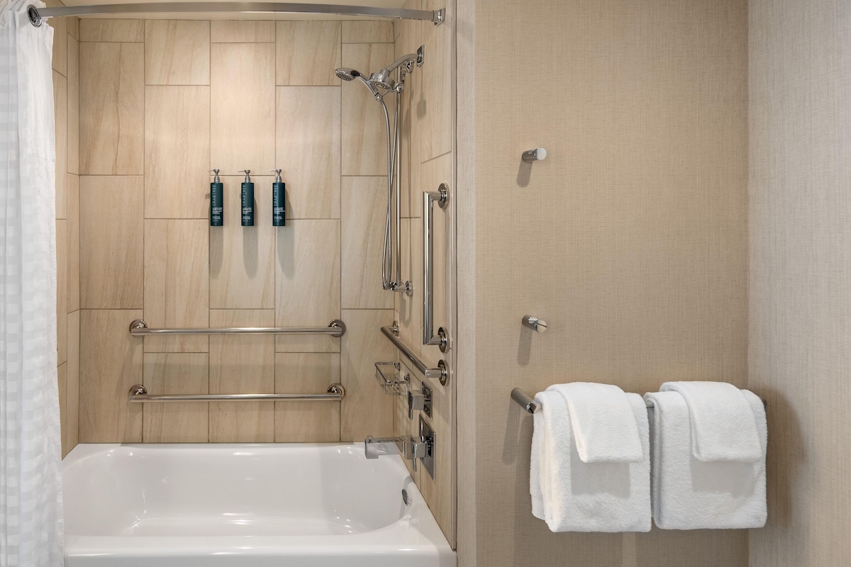 Ein modernes Badezimmer mit einer Badewanne, einer Dusche inklusive Handbrause und zwei Shampooflaschen an der Wand.