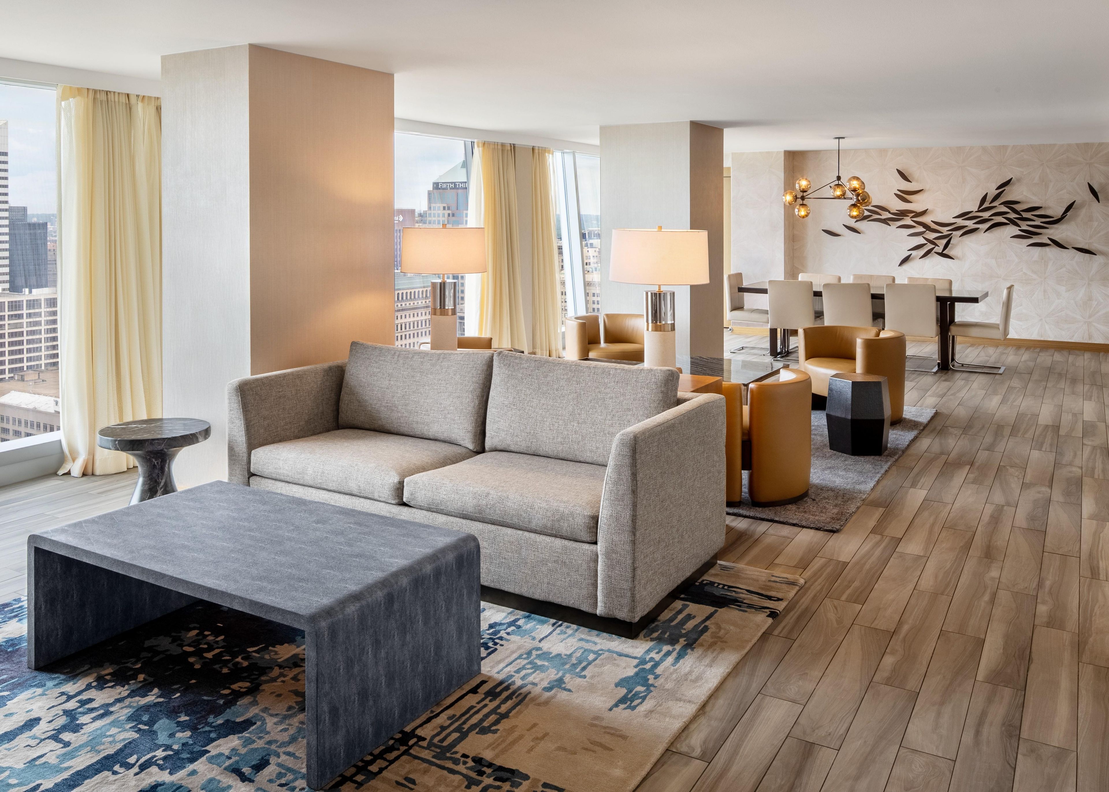 A modern hotel lobby with a sofa, armchairs, a coffee table, and a dining area.