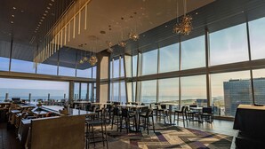 A modern dining area with large windows, high ceilings, and contemporary lighting fixtures. - Hilton Cleveland Downtown (Cleveland)