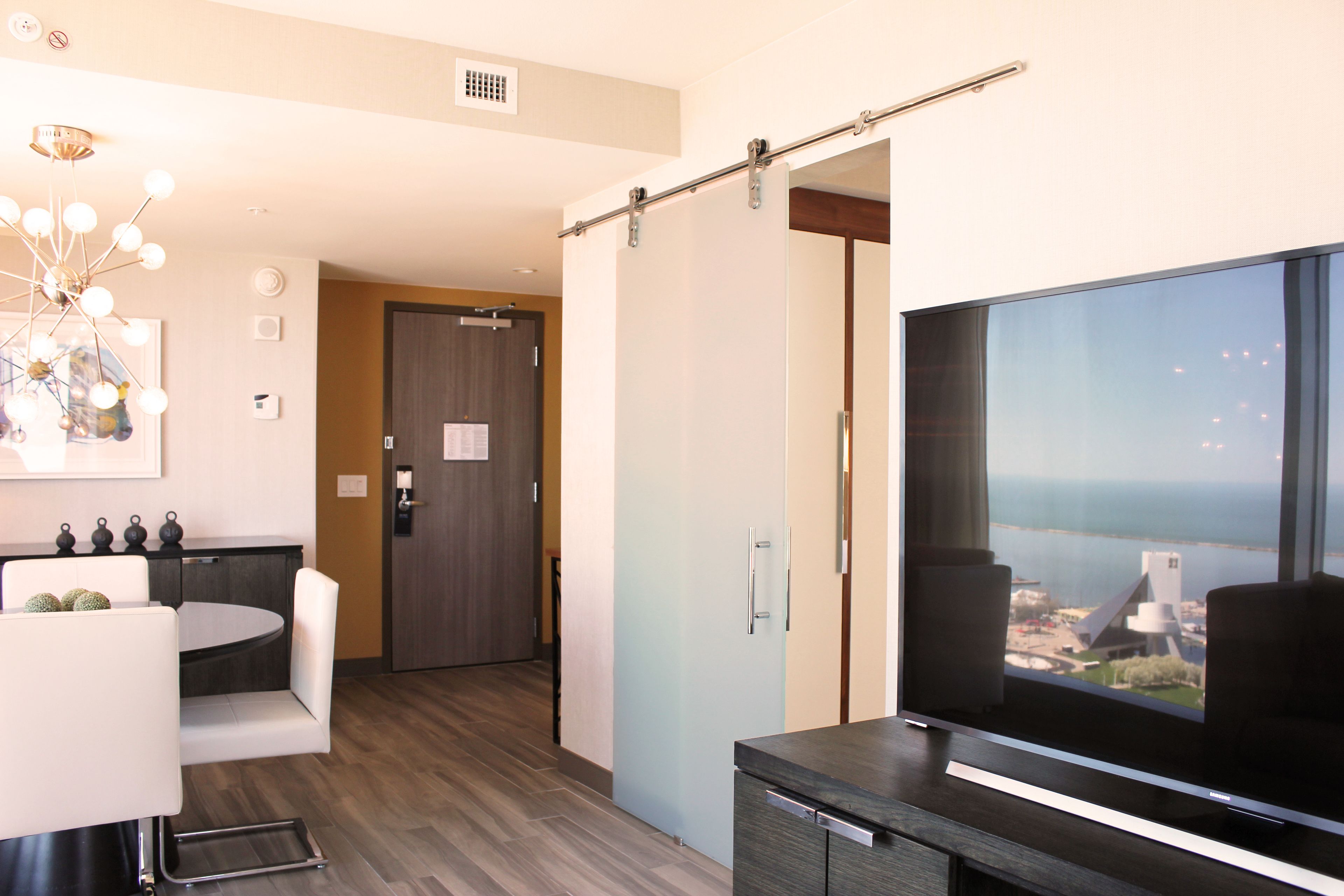 Ein modernes Wohnzimmer mit großem Fernseher, Essbereich und Blick auf die Stadt durch ein großes Fenster.