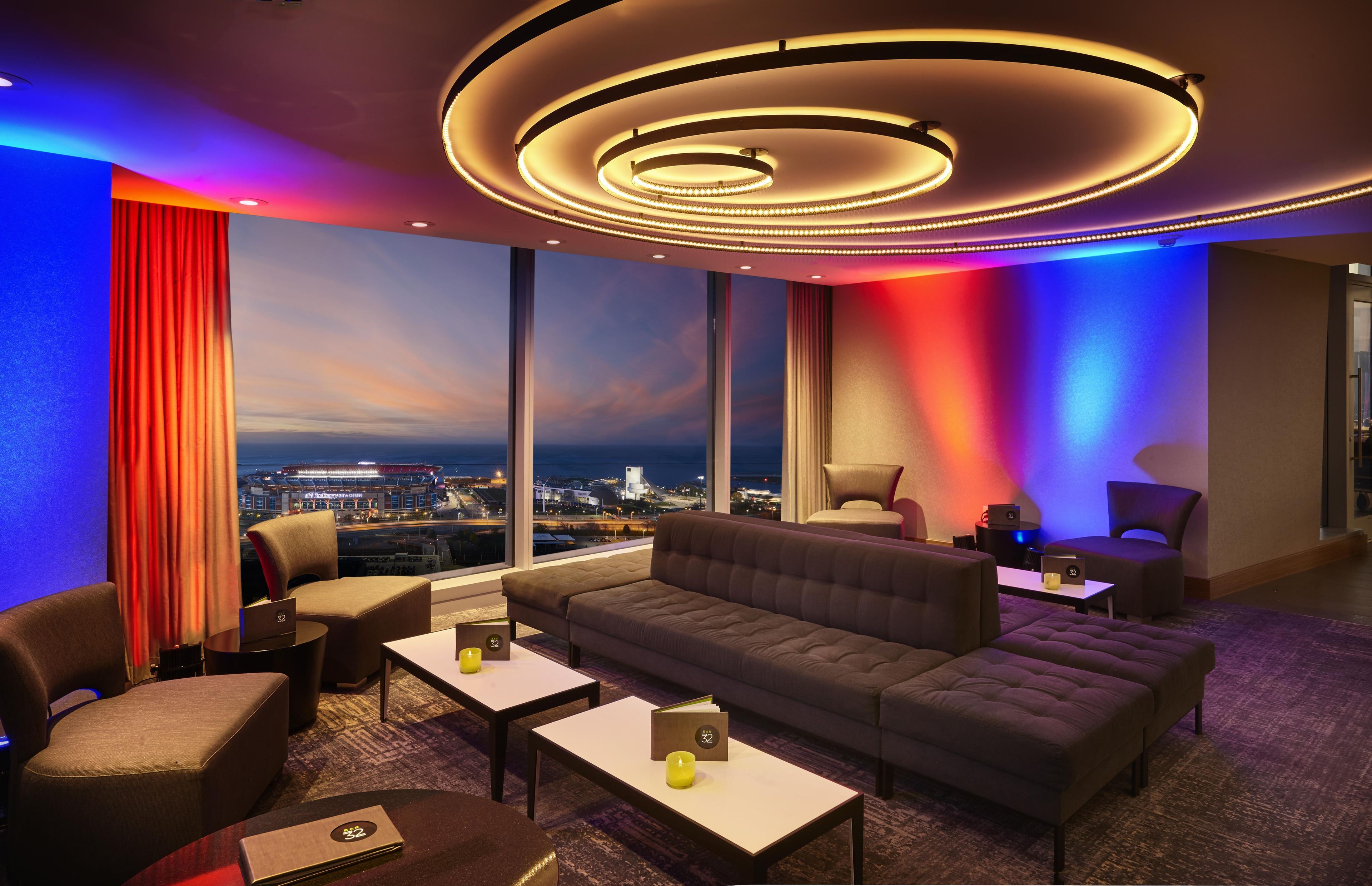 A modern lounge with a sofa, armchairs, and a coffee table. Large windows offer a city view.