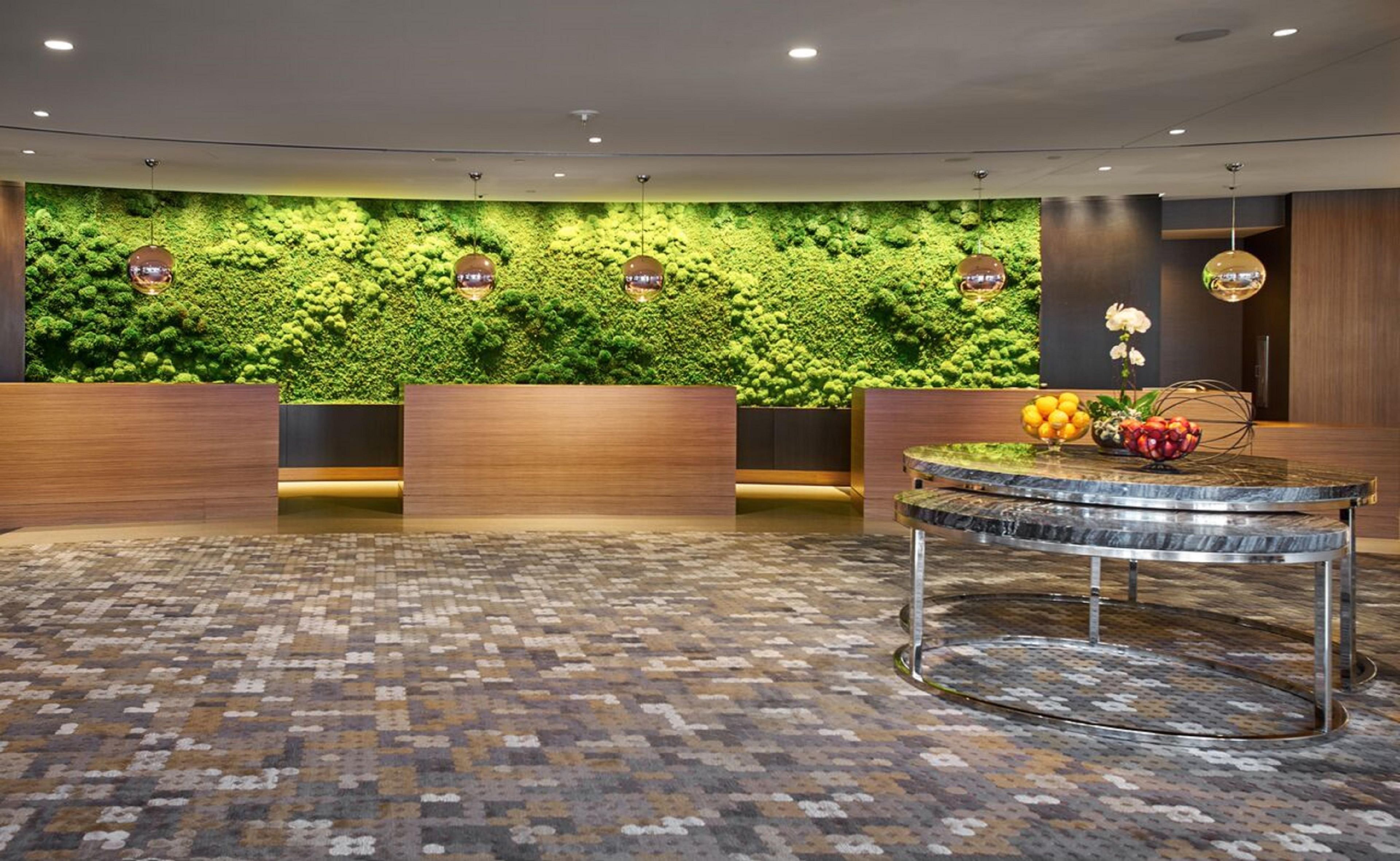 A reception area with a green wall, wooden reception desks, and a marble table with fruit.