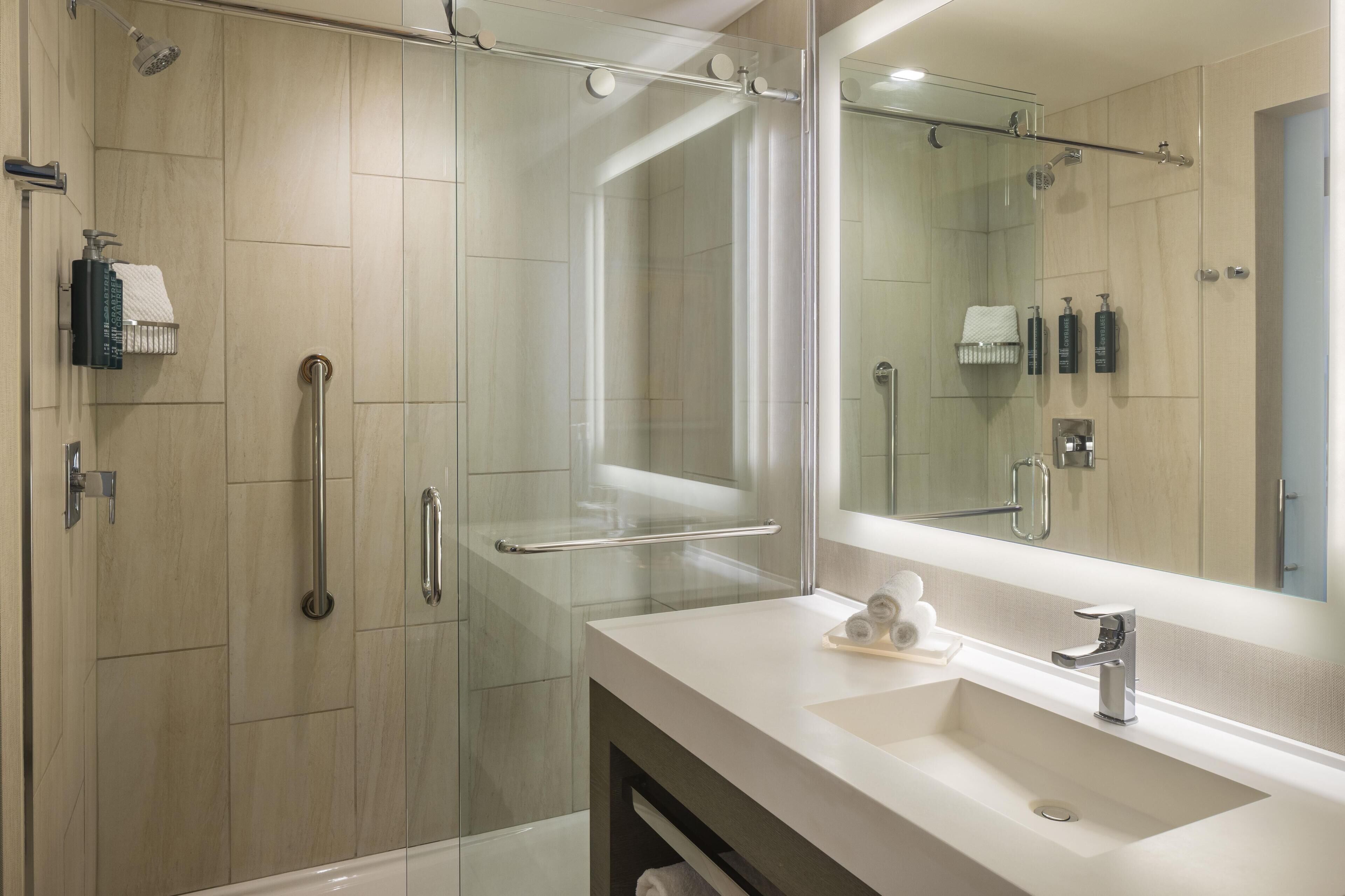 Een moderne badkamer met een douchecabine van glas, een grote spiegel en een witte wastafel.