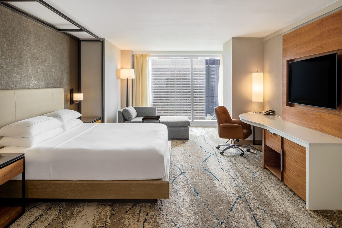 Ein Hotelzimmer mit einem großen Bett, einem Schreibtisch, einem Sessel und einem Fernseher.