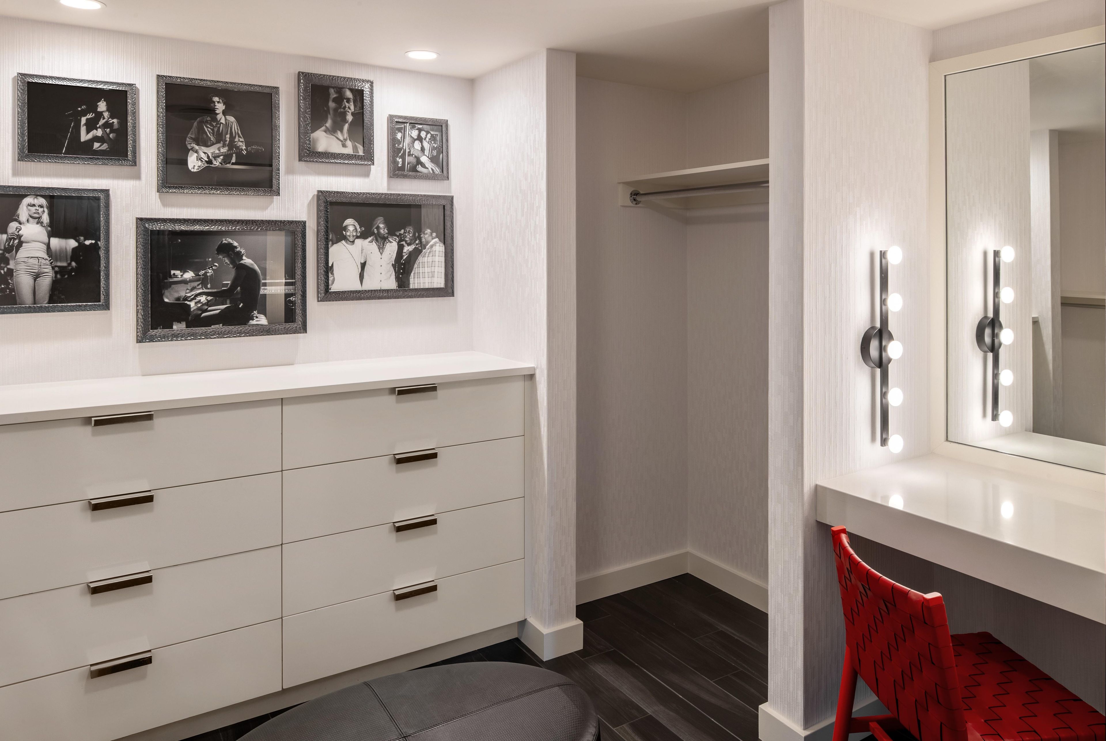 A bathroom with a vanity, a mirror with lights, and framed pictures on the wall.