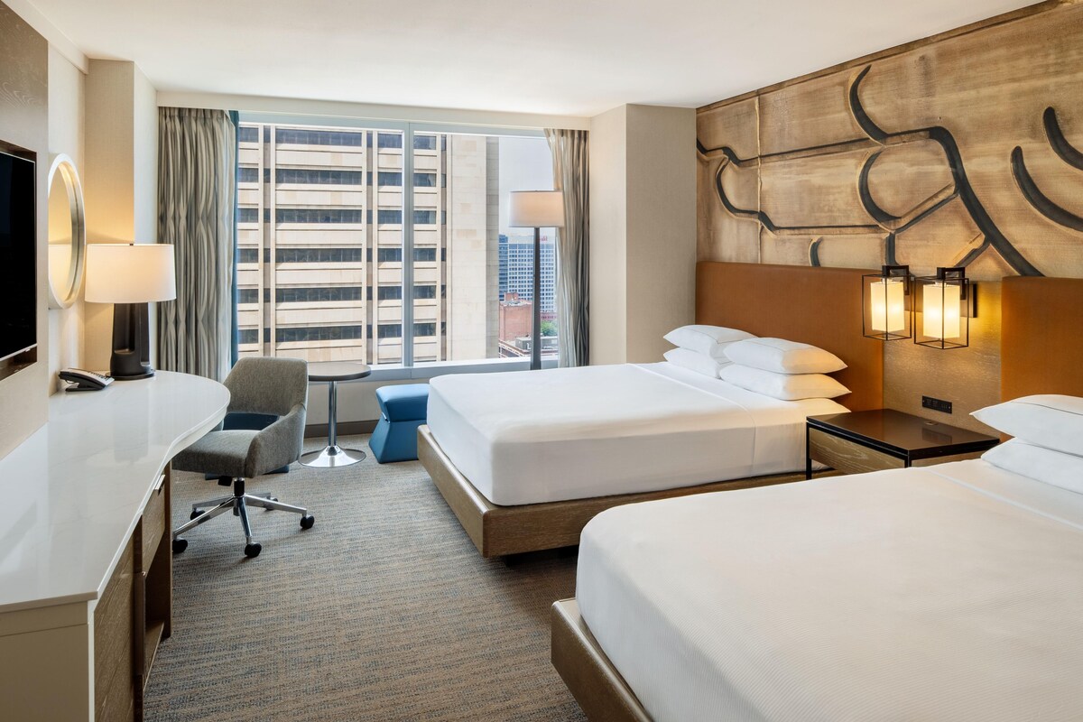 Ein Hotelzimmer mit einem großen Bett, einem Schreibtisch mit Stuhl, einem kleinen Tisch und einem Fernseher.