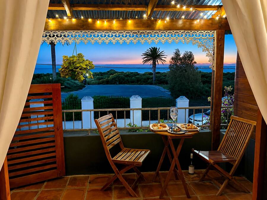 A balcony with two wooden chairs, a table with plates and a glass, and a view of the landscape.